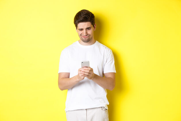 黄色那个家伙不高兴地看着智能手机屏幕 读着手机上奇怪的信息 站在白色t年轻移动时尚