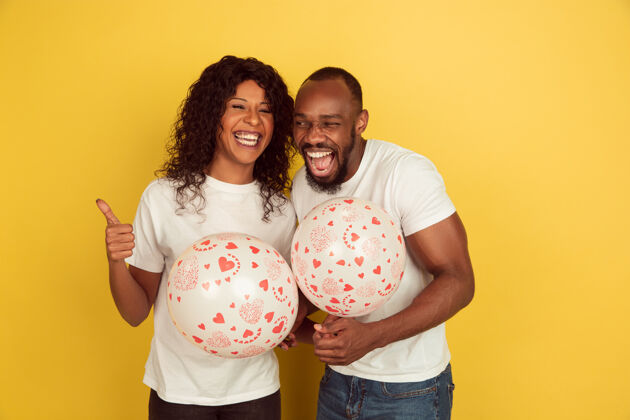 面部举着气球情人节庆祝 快乐的非洲裔美国夫妇被隔离在黄色的墙上人类情感的概念 面部表情 爱情 关系 浪漫的节日表情情人浪漫
