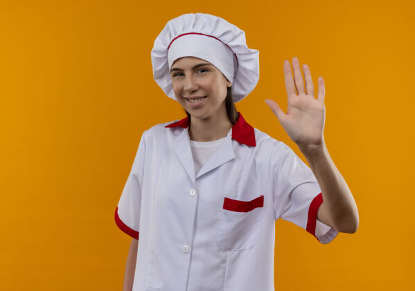 烹饪身着厨师制服的年轻快乐的白人厨师女孩在橘子上举手并留有复印空间提高空间年轻