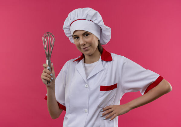 复制穿着厨师制服的年轻快乐的白人厨师女孩拿着威士忌 把手放在腰上 粉色的有复印空间拿着厨师拂
