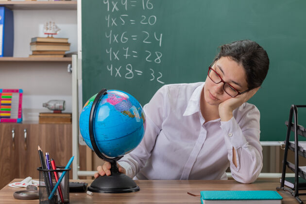 坐着年轻的女老师戴着眼镜拿着地球仪看着它累了眼镜女人地球仪