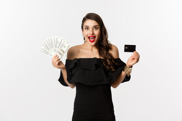 美丽时尚购物理念兴奋的黑衣女人 展示信用卡和美元 微笑着盯着相机 白色背景女性口红服饰