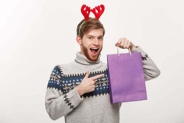 欢呼年轻帅气的胡须男高兴地拿着购物袋在手上孤立着白色年轻包圣诞节
