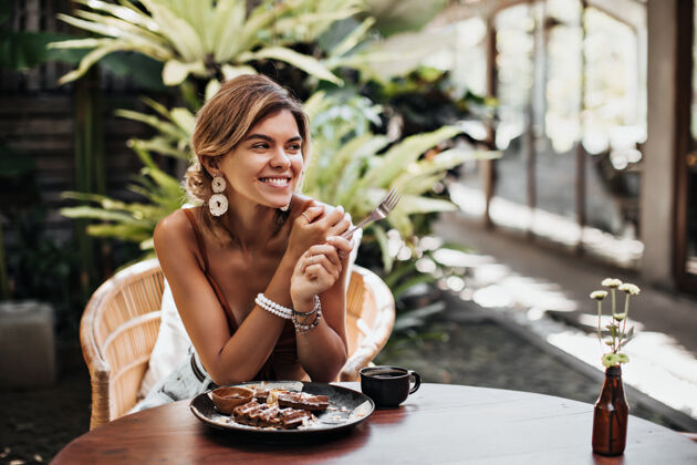 自然夏天 穿着棕色胸罩 戴着白色大耳环的开朗女人在街上的咖啡馆里尽情地笑着休息女人美丽黑发