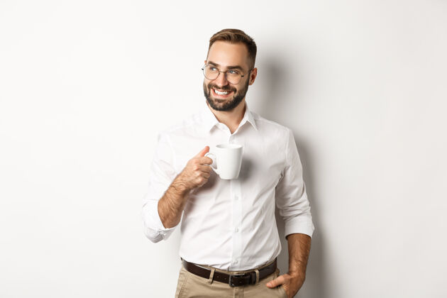 男性成功的商人喝着咖啡 满脸满意的微笑 站在白色的背景上杯子工人年轻