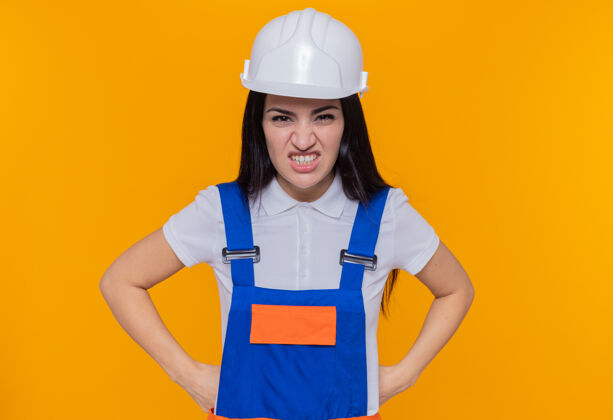 女人年轻的建筑女工穿着建筑制服 戴着安全帽看着摄像机臀部愤怒建筑
