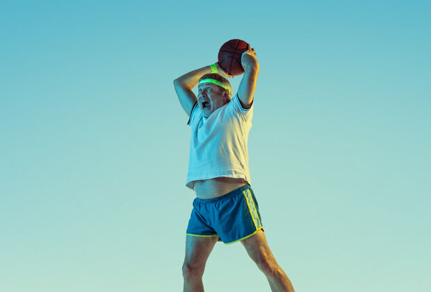 网球拍高级男子在霓虹灯下的斜坡墙上打篮球身材魁梧的白种人男模保持活跃 运动运动 活动 运动 幸福 健康的生活方式的概念球动作业余