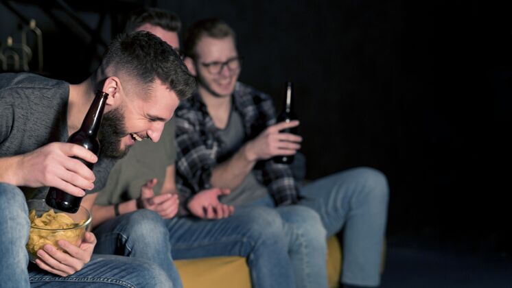 同志笑脸男朋友一起看电视上的体育节目 一边吃零食和啤酒哥们电视电视