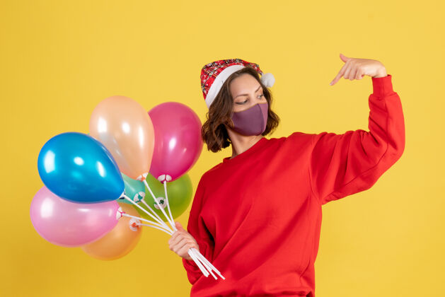外科面具正面图：戴着面具手持气球的年轻女子在黄色庆祝派对上感慨新年的女人正面飞机派对