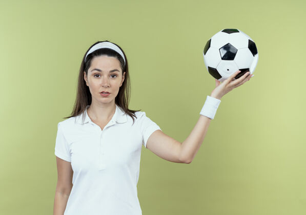头带戴着头巾的年轻健身女 手拿足球 严肃的脸站在轻墙上立场举行年轻