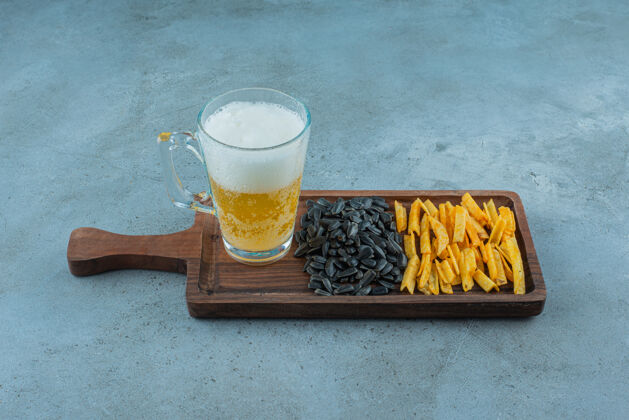 新鲜土豆条 葵花籽和一杯啤酒放在一块板上 蓝色背景美味美味啤酒