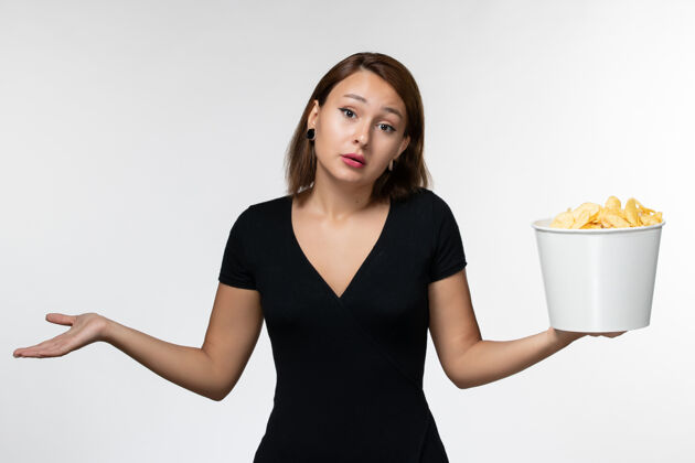 电影正面图身穿黑色衬衫的年轻女性在白色表面上拿着薯片举行土豆衬衫