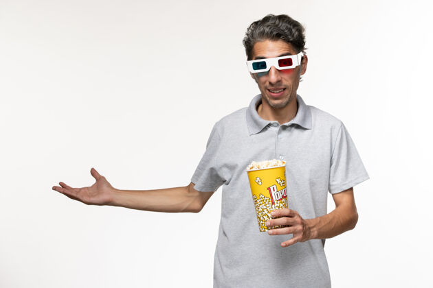前面正面图：戴着d型太阳镜的年轻男性手持爆米花站在白色的地面上电影院男电影