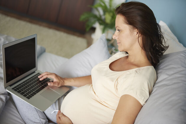 工作孕妇在床上使用笔记本电脑后代床母亲