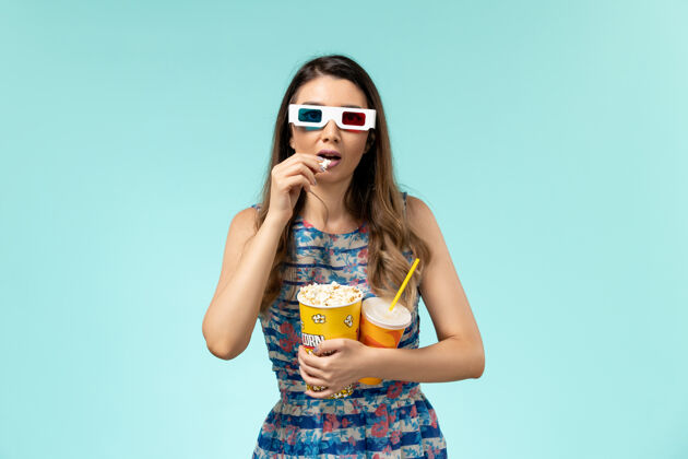 剧院正面图年轻女性拿着爆米花包 戴着d墨镜在蓝色表面喝酒性感电影包装