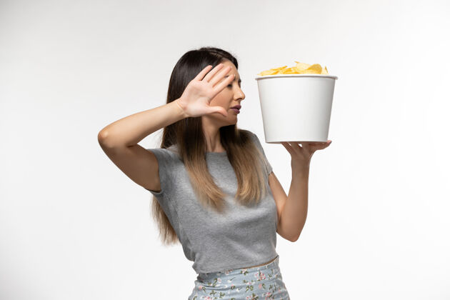 年轻的女性正面图：年轻女性手持薯片在白色表面上看电影孤独电影土豆