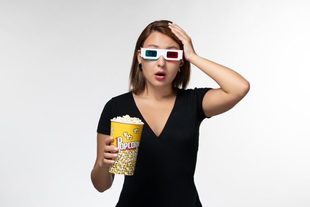 孤独正面图：年轻女性戴着d型太阳镜拿着爆米花包 在白色表面上看电影太阳镜性感年轻女性
