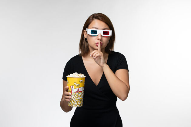 前面正面图：年轻女性戴着d型太阳镜拿着爆米花包 在白色书桌上看电影电影院抱着包装