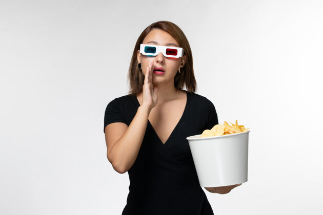 女士正面图年轻女性戴着d型太阳镜拿着薯片 在浅白的表面上看电影抱太阳镜浅白色