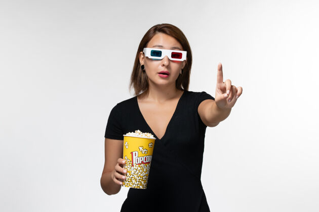 漂亮正面图年轻女性戴着d型太阳镜拿着爆米花 在白色表面上看电影女士电影院爆米花