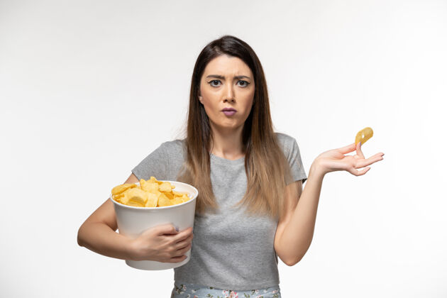 土豆正面图：年轻女性手持薯片在白色表面上看电影电影前面孤独