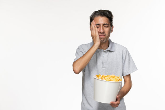 年轻的男正面图：年轻男性在白色桌子上吃薯片前面孤独电影