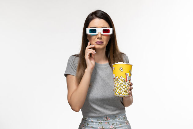 爆米花正面图年轻女性手持爆米花 戴着d型太阳镜在浅白色的表面上看电影年轻的女性抱着太阳镜