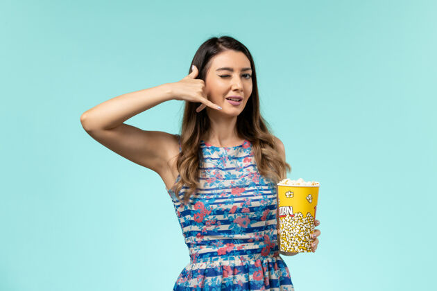 爆米花正面图年轻女性手持爆米花包 在蓝色表面摆姿势姿势电影女士