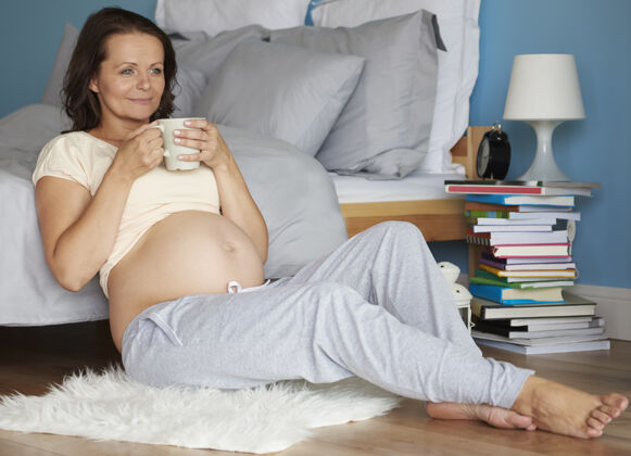 喝酒怀孕最后一个月的女人坐着地板期待