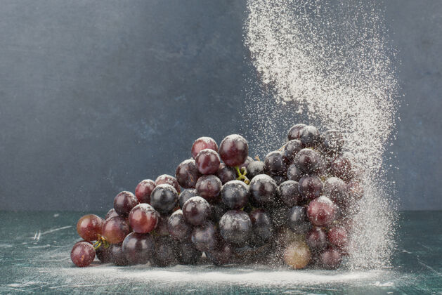 粉大理石桌上挂着一束用粉末装饰的黑葡萄成熟水果簇