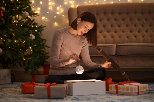 女性漂亮的黑发女人拿着一个白色的圣诞球打开一个可爱的礼物礼品盒灯梦