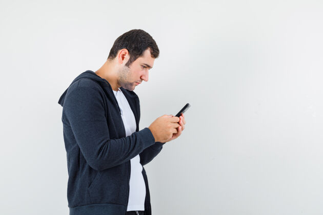 时尚男青年穿着t恤衫 夹克衫 用手机 看上去很忙 前视图一个胡须手
