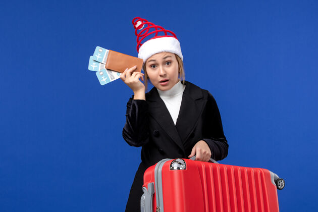 成功正面图年轻女性手持包和机票在蓝墙飞机假日之旅商人举行帽子