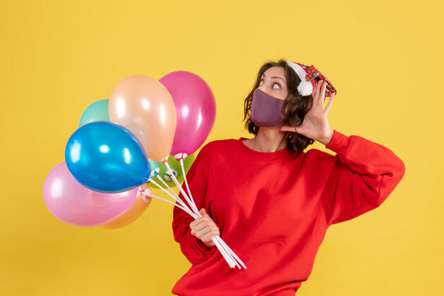 颜色正面图戴着面具手持气球的年轻女子聆听黄色庆典派对情感新年彩女正面情感年轻女人