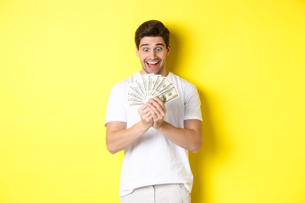 男性快乐的男人看着钱 微笑着兴奋 中奖了 拿到了银行贷款 站在黄色的背景下金钱黄色成年人