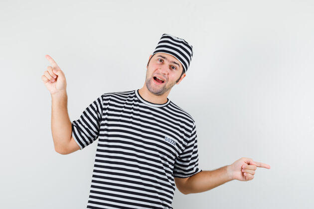 一个年轻的男子指着t恤衫 帽子和快乐的样子 前面的看法姿势男人指向