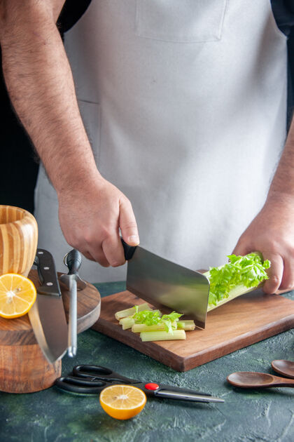 男人正面图男厨师在深色餐桌上切芹菜沙拉减肥餐彩色照片食物健康颜色沙拉设备