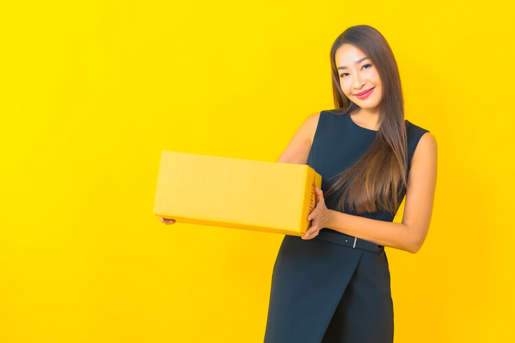 年轻人肖像美丽的年轻亚洲女商人与棕色盒子准备在黄色背景上运输微笑盒子包