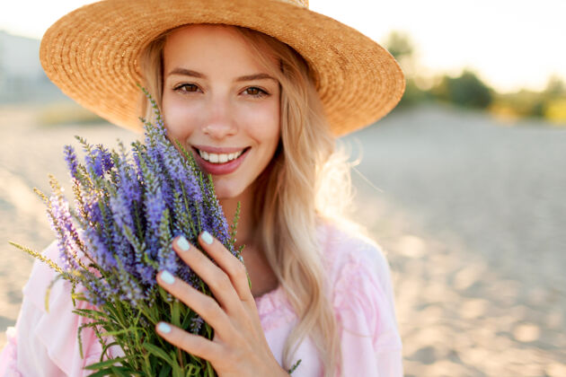 花微笑着戴草帽的漂亮女人在海边阳光明媚的海滩上摆着一束鲜花特写肖像健康脸衣服