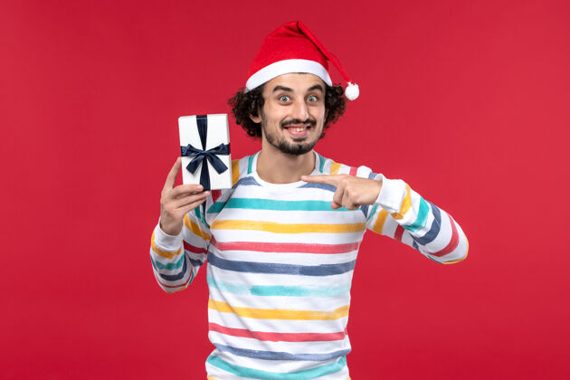 年轻的男性正面图：年轻男性手持小礼物 红色背景 红色节日 新年情绪小玩家情感