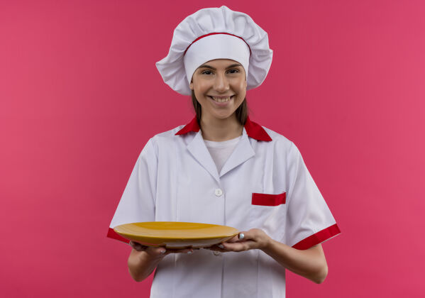 女孩身着厨师制服 面带微笑的白人年轻厨师女孩拿着盘子隔离在粉色空间和复印空间厨师年轻制服