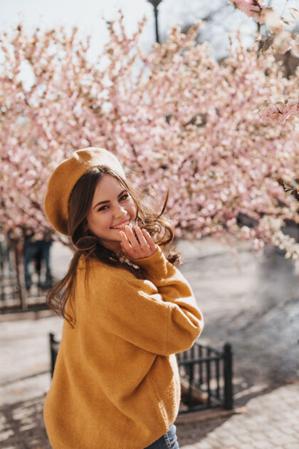 温柔的花可爱的女人穿着时尚的橙色服装 在樱花的背景下笑着迷人的女士穿着卡什米尔毛衣和贝雷帽 微笑着在公园里散步年轻帽子衣服