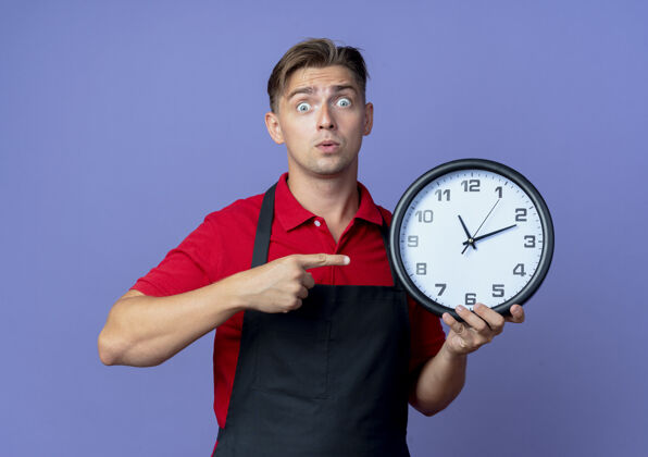 男性年轻的金发男理发师穿着制服 拿着一只钟 指着紫色的空间里的复制空间制服时钟复制