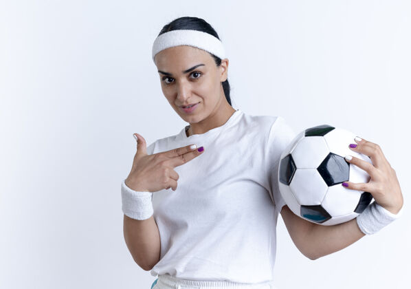 穿年轻自信的高加索运动女性戴着头带和腕带拿着并指向球 在空白处与复制空间隔离复制腕带点