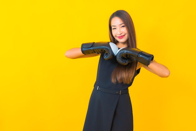 锻炼在黄色背景上画一个戴拳击手套的美丽的亚洲女商人健身冠军肖像