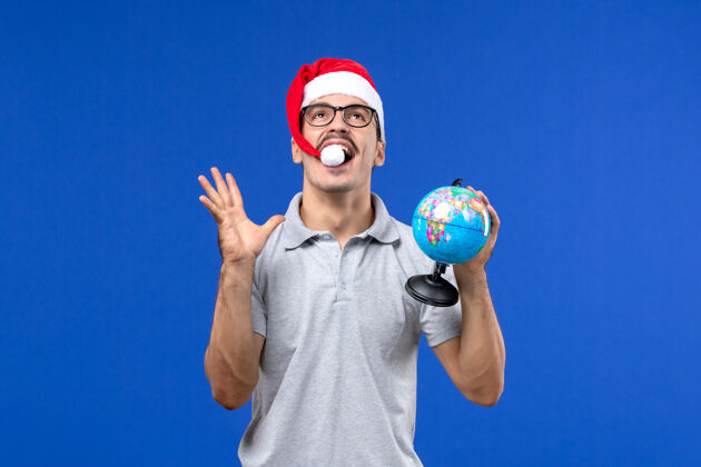 体育正面图年轻的男性手持地球仪在蓝色的墙壁上度假旅行男性前面圣诞节年轻男性