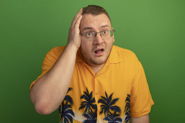 人一个戴着眼镜 穿着橘色衬衫的男人一边看一边 一边困惑地把手放在头上 因为他错站在绿色的墙上了头眼镜站