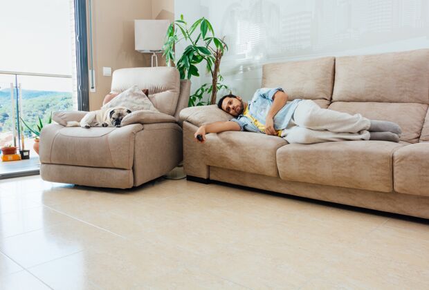 现代一个看起来很无聊 很累的年轻人拿着电视遥控器 躺在沙发上人自然女人