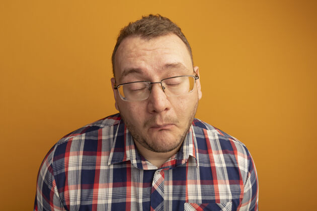 悲伤一个戴着眼镜 穿着格子衬衫 表情悲伤的男人站在橙色的墙上不快乐站立男人