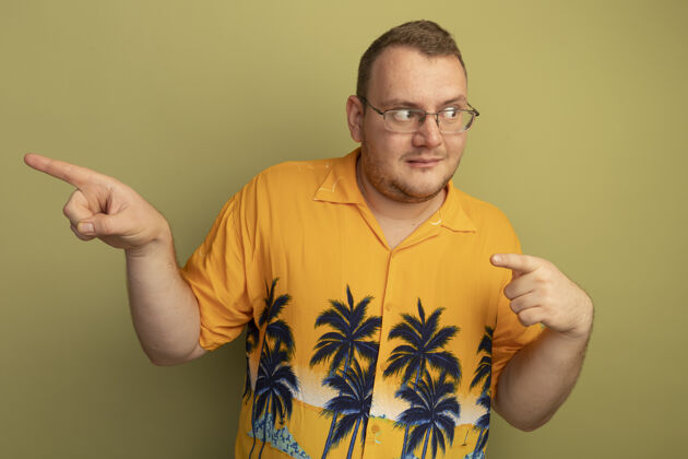 表情一个戴着眼镜 身穿橘色衬衫的男人 带着怀疑的表情 用食指指着站在绿色墙壁上的一边眼镜站手指